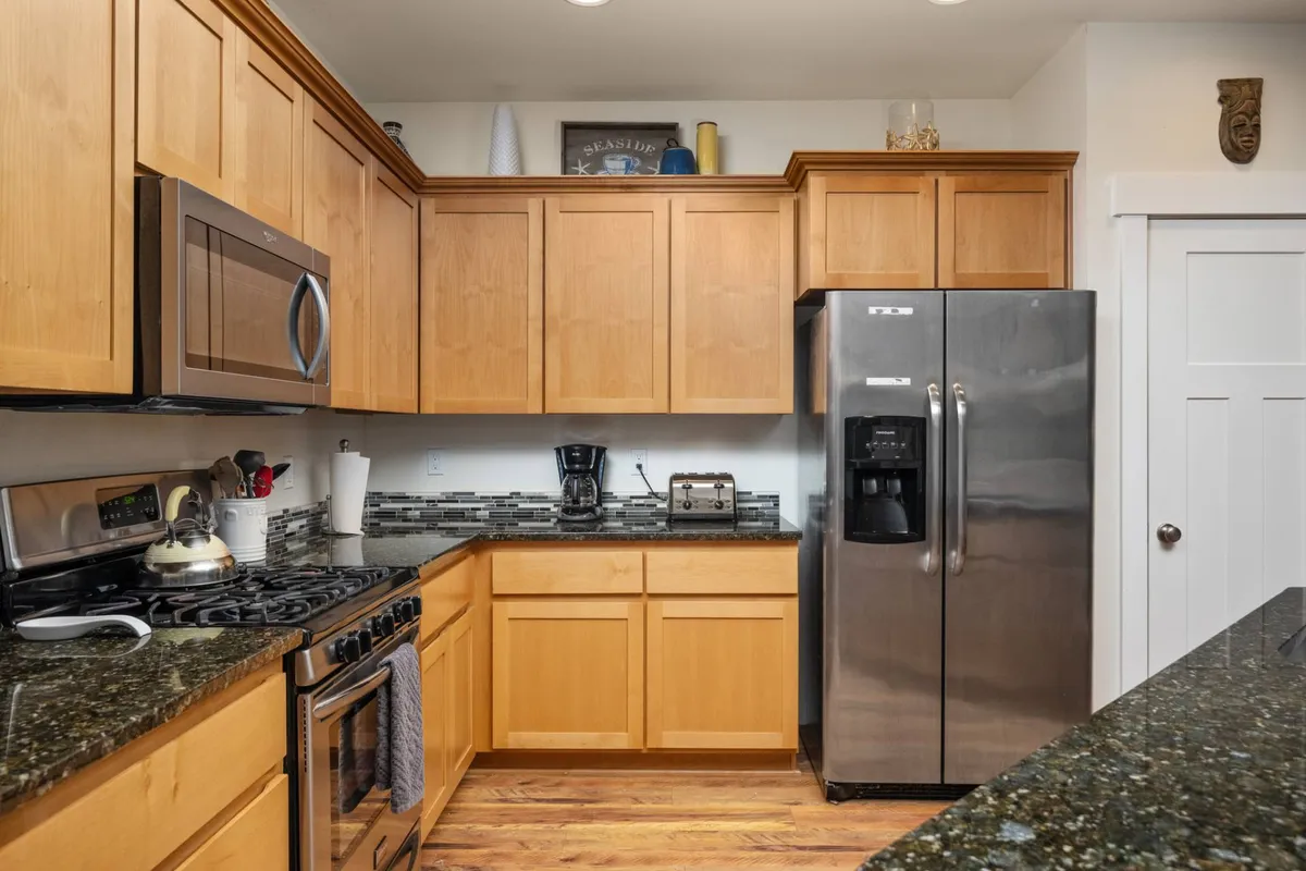 This image showcases a bright, homey kitchen featuring a stainless steel refrigerator, granite countertops, wooden cabinets, and visible kitchen appliances. The scene feels lively and practical, suggesting both everyday cooking and special gatherings.