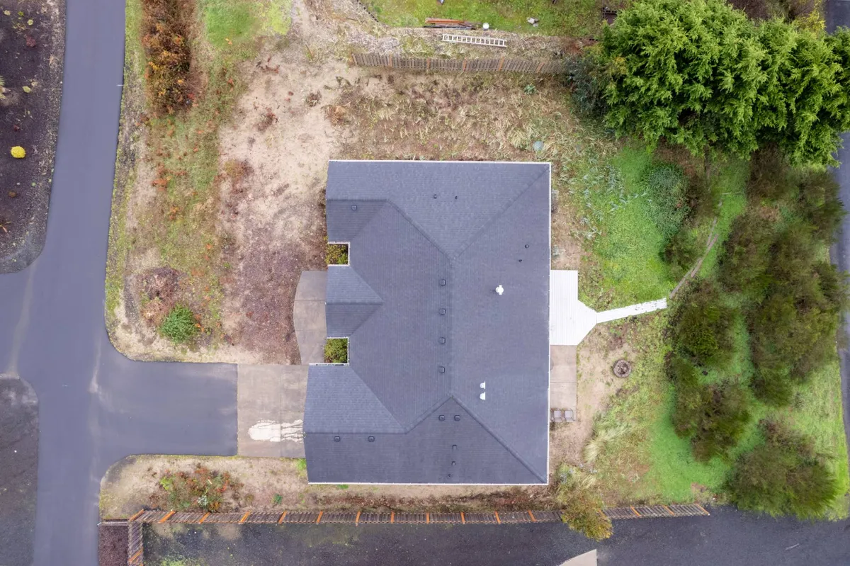An exterior view of the home, focusing on the roof structure and surrounding greenery, with a driveway leading up to the property. The peaceful yard sets the scene for mornings or evenings enjoying the outdoors just steps from the home.