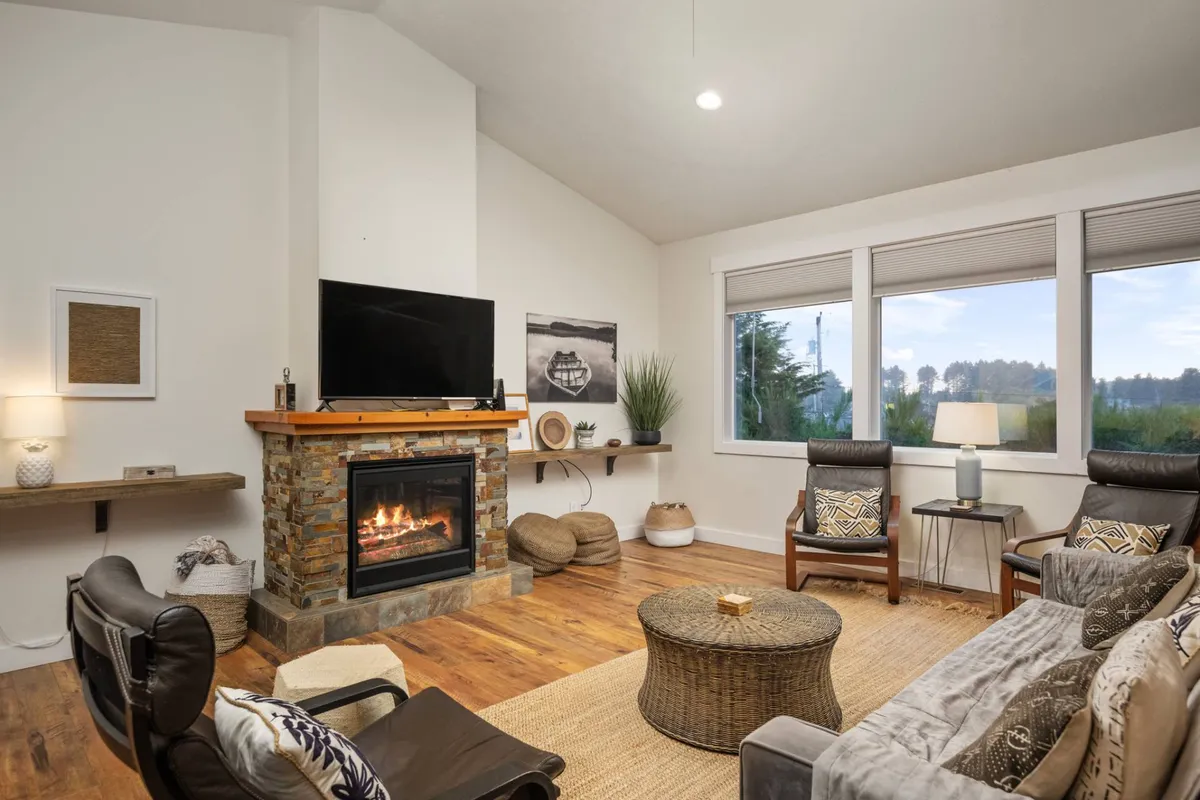 A welcoming living area with a sleek fireplace, large windows that let in abundant sunlight, a comfortable sofa, and a television. The room offers panoramic lake views beyond the windows and is designed for both relaxation and intimate gatherings.