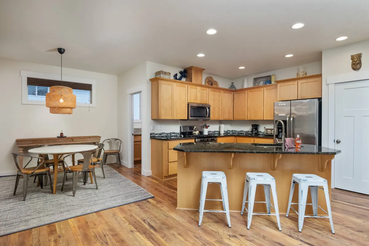 A kitchen island and adjacent dining table sit beneath a stylish light fixture in an inviting, open-plan setting. The image emphasizes the fluid transition between kitchen and dining areas, embodying an atmosphere that encourages group gatherings and casual breakfasts.
