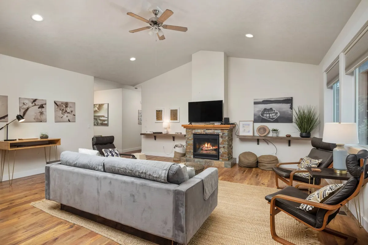 A spacious living room featuring a plush sofa, inviting fireplace, contemporary artwork, and comfortable chairs. The space is filled with natural light, highlighting the modern decor and cozy atmosphere designed for relaxation and socializing.