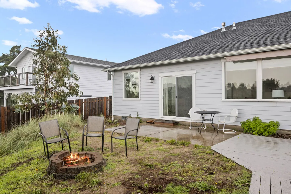 An inviting outdoor fire pit area with comfortable seating arranged around a glowing fire, adjacent to a modern sliding glass door. The ambiance suggests cozy gatherings, alfresco dining, and stargazing under the open sky.